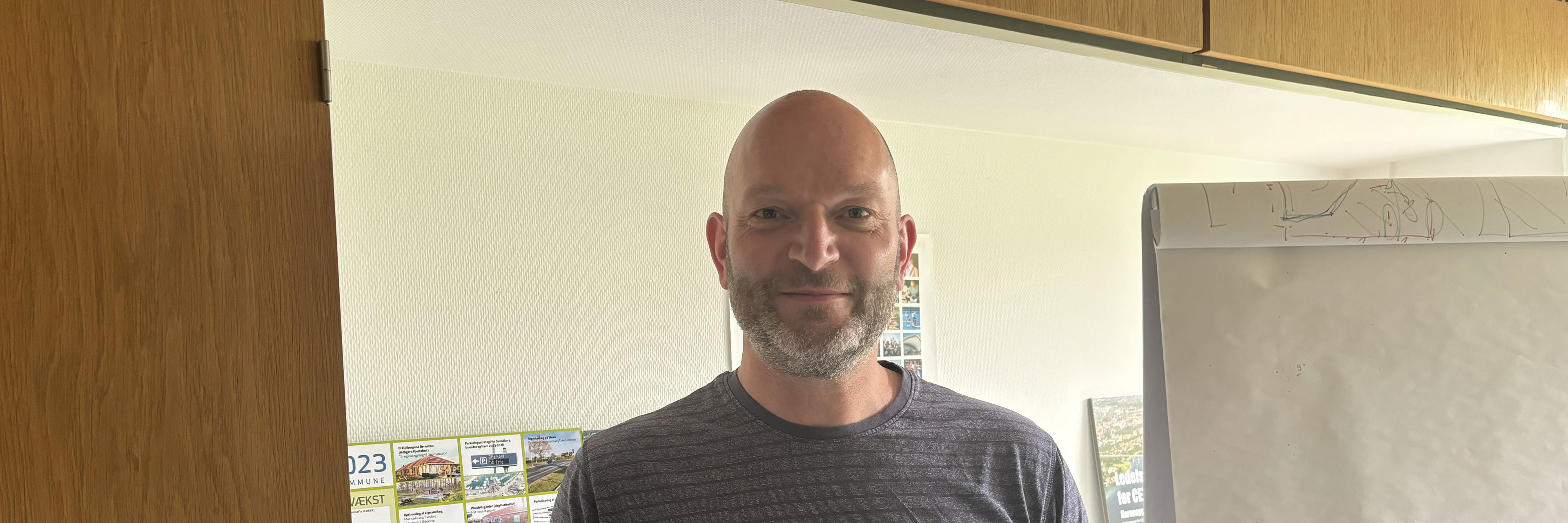 Midaldrende mand med skæg, som står foran brochurer og flipover
