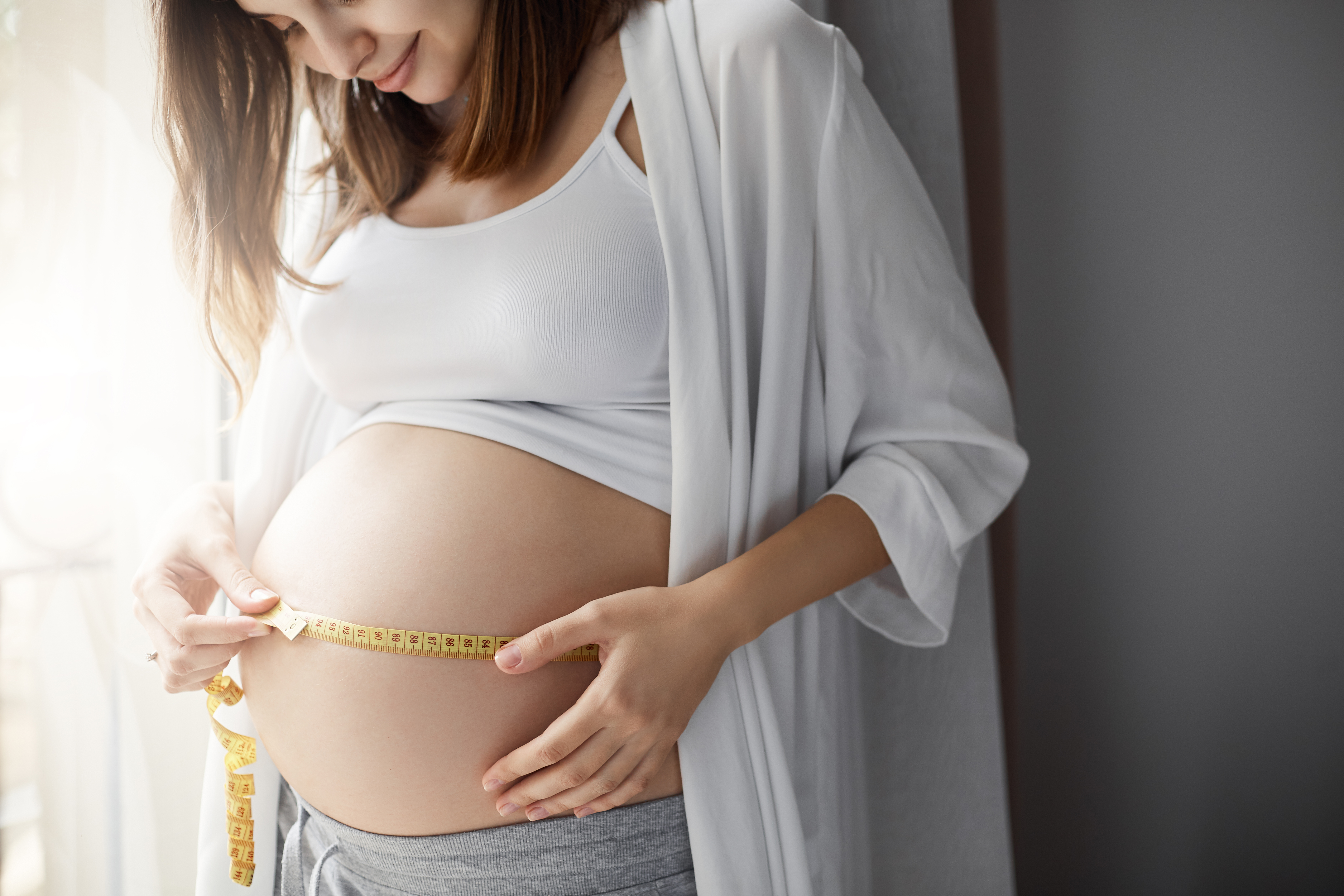 Gravid kvinde måler sin mave med en cemtimetermål
