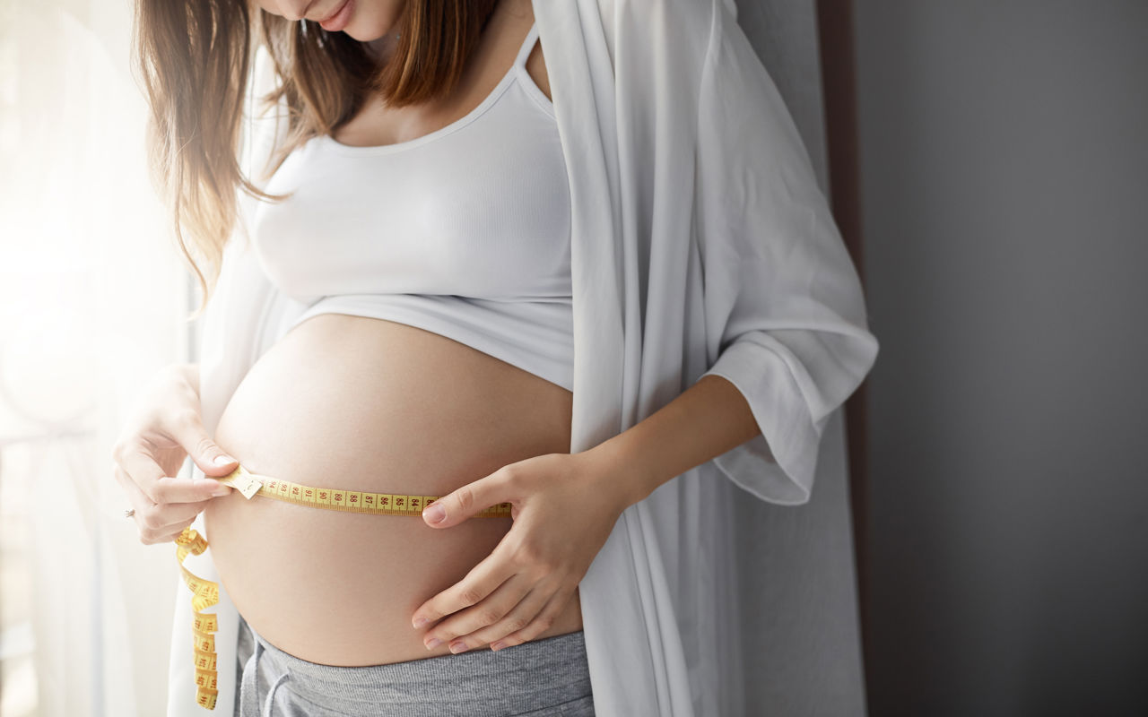 Gravid kvinde måler sin mave med en cemtimetermål