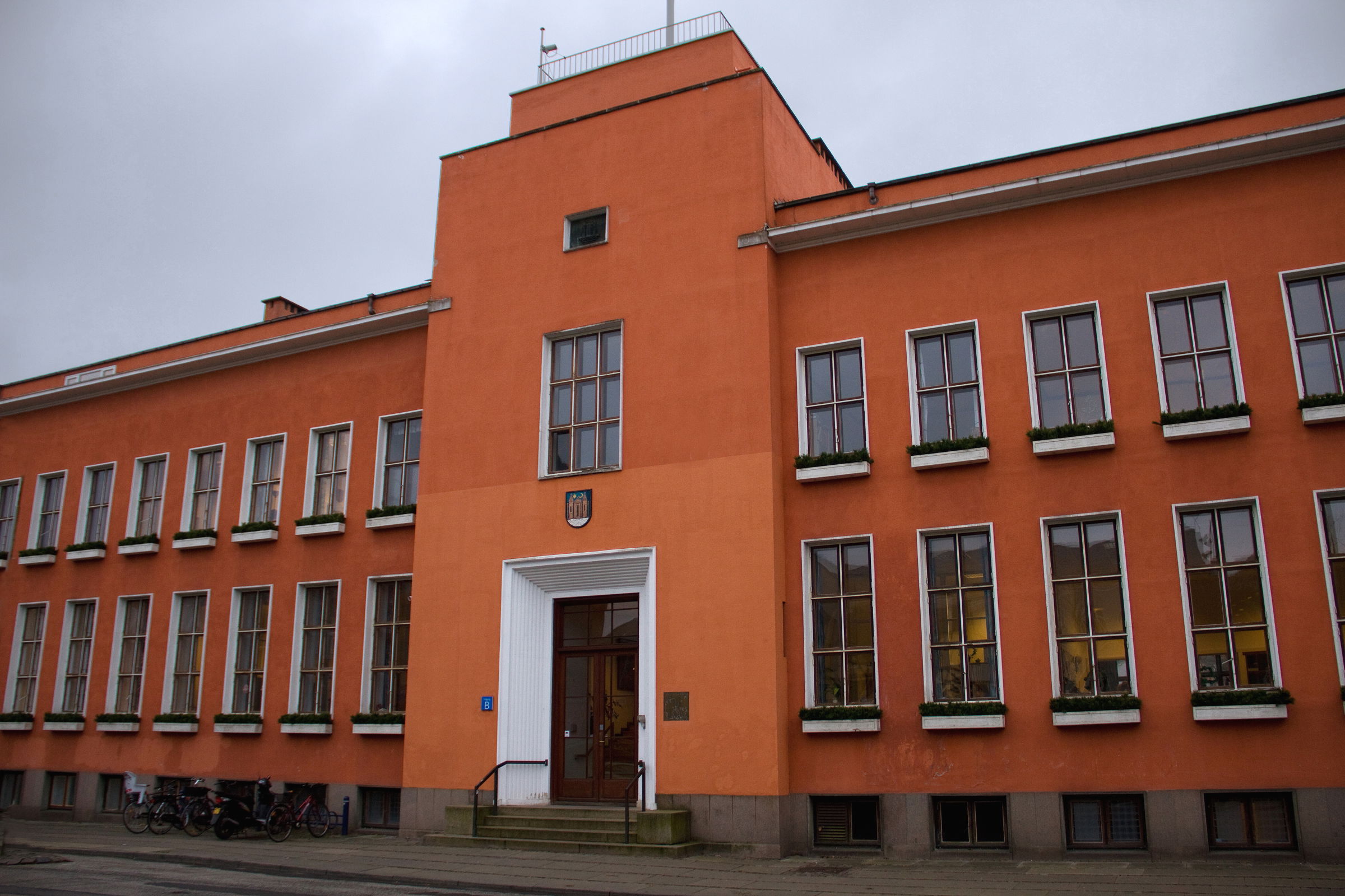 En stor rødlig bygning med brune og hvide vinduesrammer, der viser at bygningen har to etager.